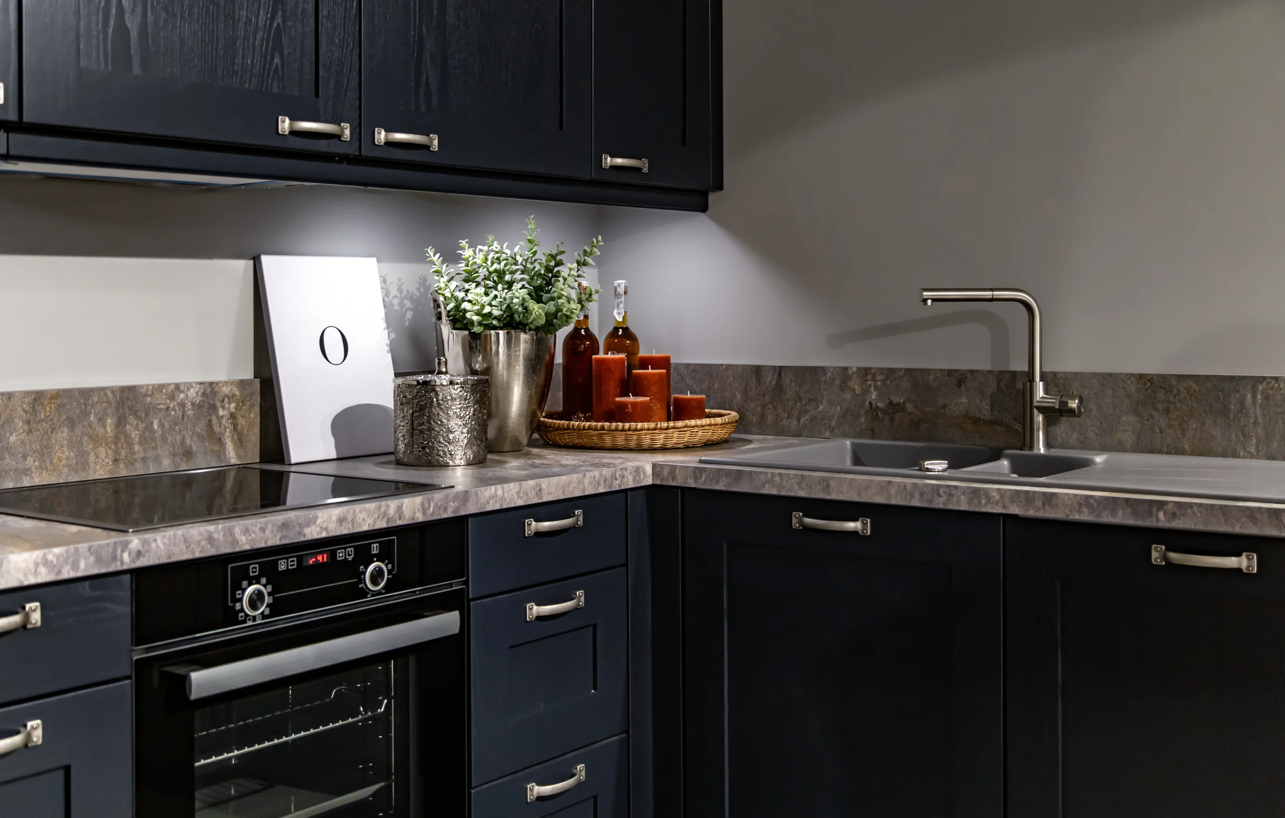 Dark navy kitchen cabinets with silver handles, grey stone countertop, under-cabinet lighting, and built-in oven.
